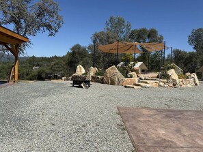 A gravel patio with a wooden pergola and a stone fire pit.