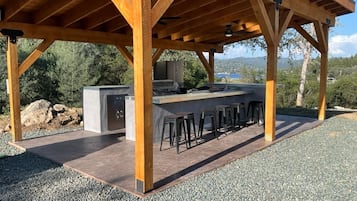 An outdoor kitchen area with a bar stool seating arrangement, a built-in grill, and a view of the surrounding landscape.