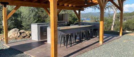 An outdoor kitchen area with a bar stool seating arrangement, a built-in grill, and a view of the surrounding landscape.