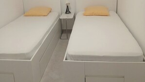 Quarto duplo com duas camas de solteiro, mesa de cabeceira e janela com persianas.