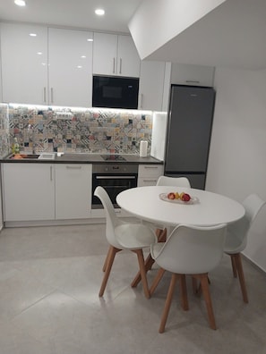 Cocina moderna con armarios blancos, salpicadero con estampado y comedor con mesa y sillas blancas.