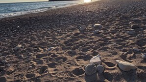 Praia com pegadas, céu claro e montanha ao longe.