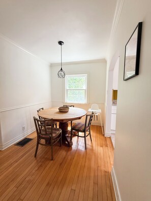 A dining area with a round wooden table, four chairs, a hanging light fixture, and a window with a view of greenery. - Cozy and Convenient - Retreat on Rosemont - Kid Friendly - Covered Back Deck (Lexington)