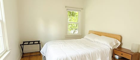 Un dormitorio con una cama individual, una mesita de noche, una ventana con vistas a zonas verdes y una alfombra estampada.