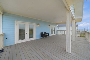 A covered deck with a light blue wall, a white door with glass panels, and a black bench. - Surfside Beach • Steps To Beach • Relax • Enjoy (Surfside Beach)