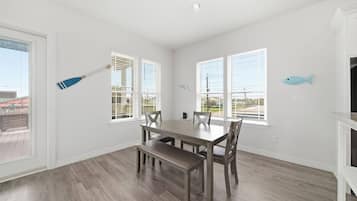 A dining area with a wooden table and chairs, large windows with blinds, and a view of the outside.
