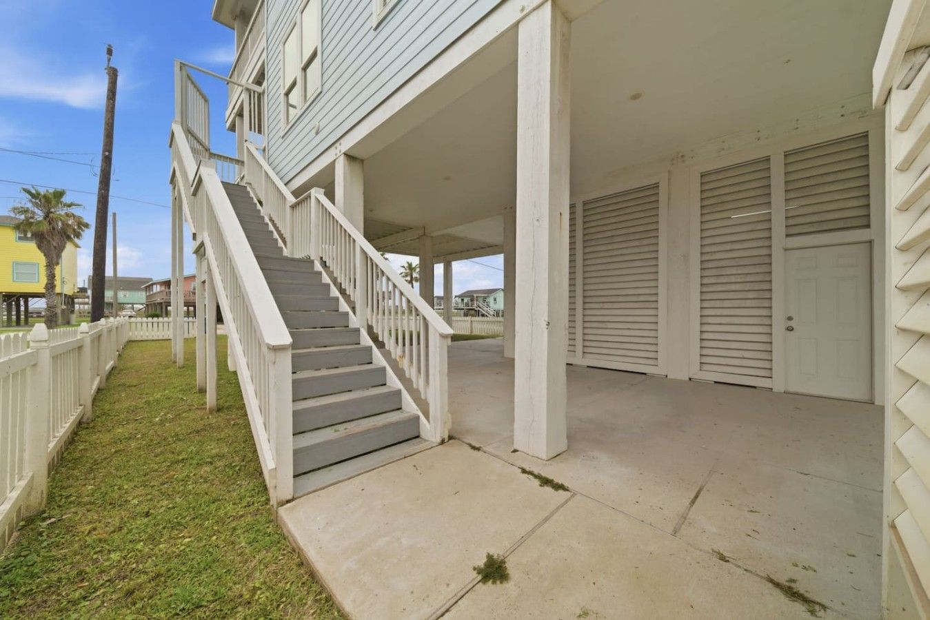 A residential building with a covered porch, a staircase, and a garage with closed doors.