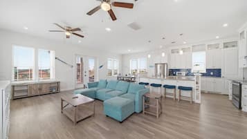 A spacious living area with a sectional sofa, a dining table with bar stools, and a kitchen with white cabinets and blue backsplash.