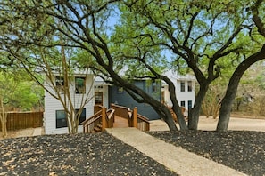 A two-story house with a wooden staircase leading to a deck, surrounded by trees and a fenced yard.