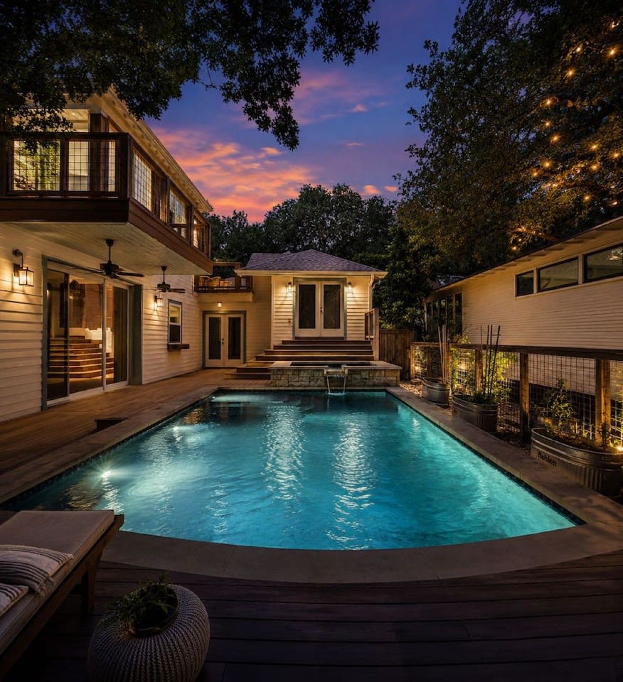Una piscina con solárium, rodeada por una casa de dos plantas con balcón e iluminación exterior.
