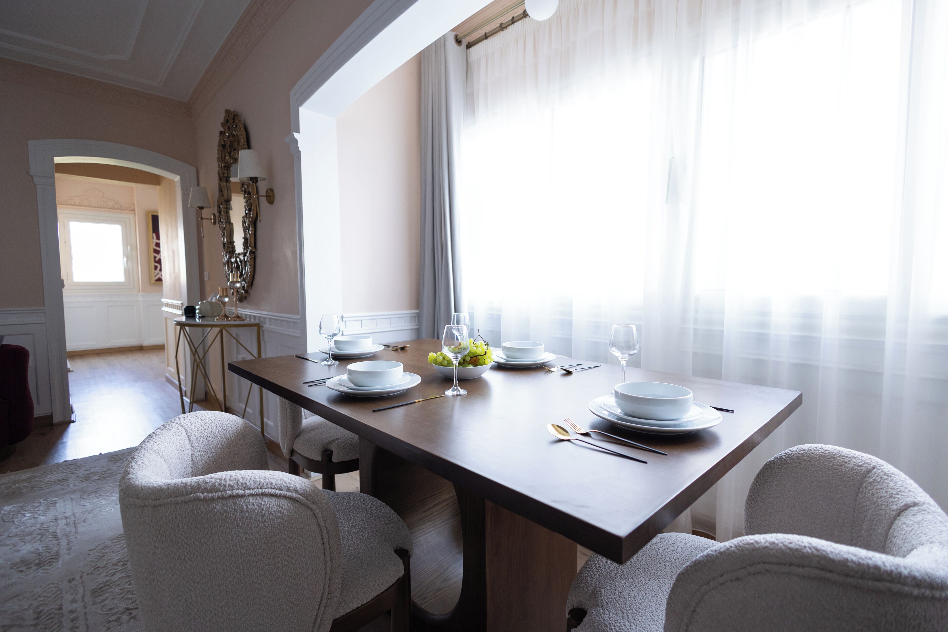 Ein Esszimmer mit einem Holztisch, gedeckt für vier Personen, weißen Stühlen und Blick auf einen Flur.