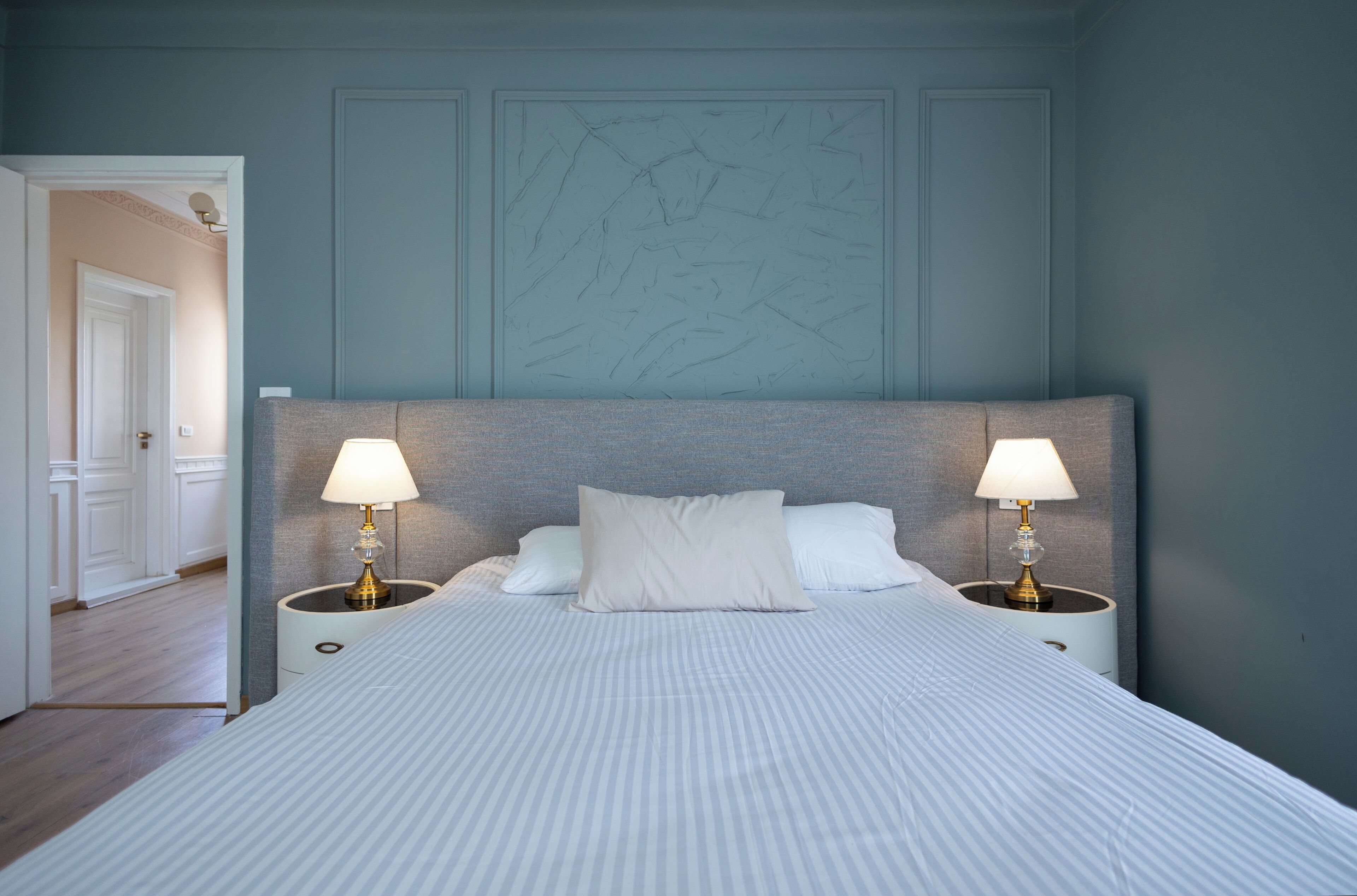 A hotel room with a large bed, two bedside lamps, and a door leading to another room.
