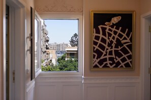 Ein Flur mit Fensterblick auf eine Stadtansicht, einer Tür mit dekorativer Verkleidung und einem gerahmten Kunstwerk an der Wand.