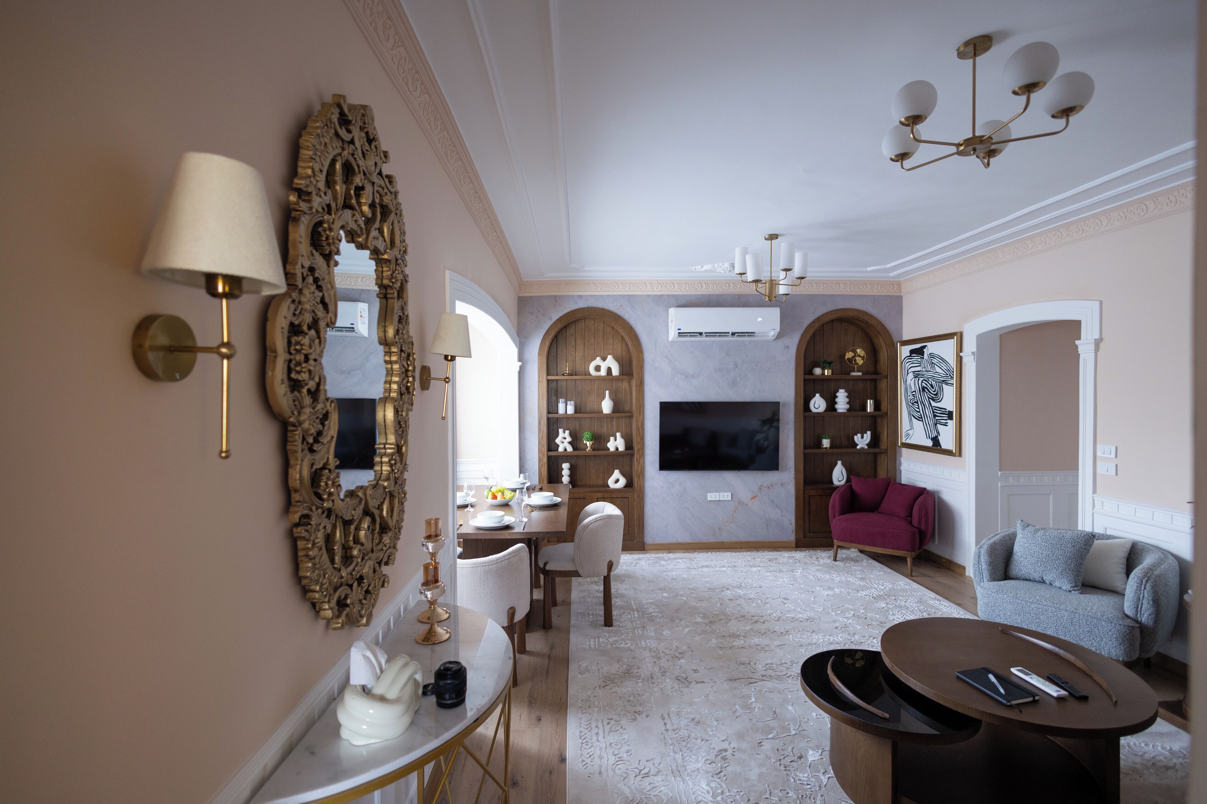 A well-lit living room with a dining area, a large ornate mirror, and a modern chandelier.