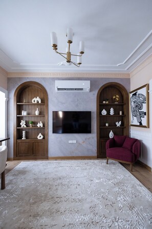 A living room with a flat-screen TV mounted on the wall, wooden shelving units, a red sofa, and a patterned rug. - Sunny Zamalek 2-Bedroom/2Bath Apartment with Side Nile View (Giza Governorate)