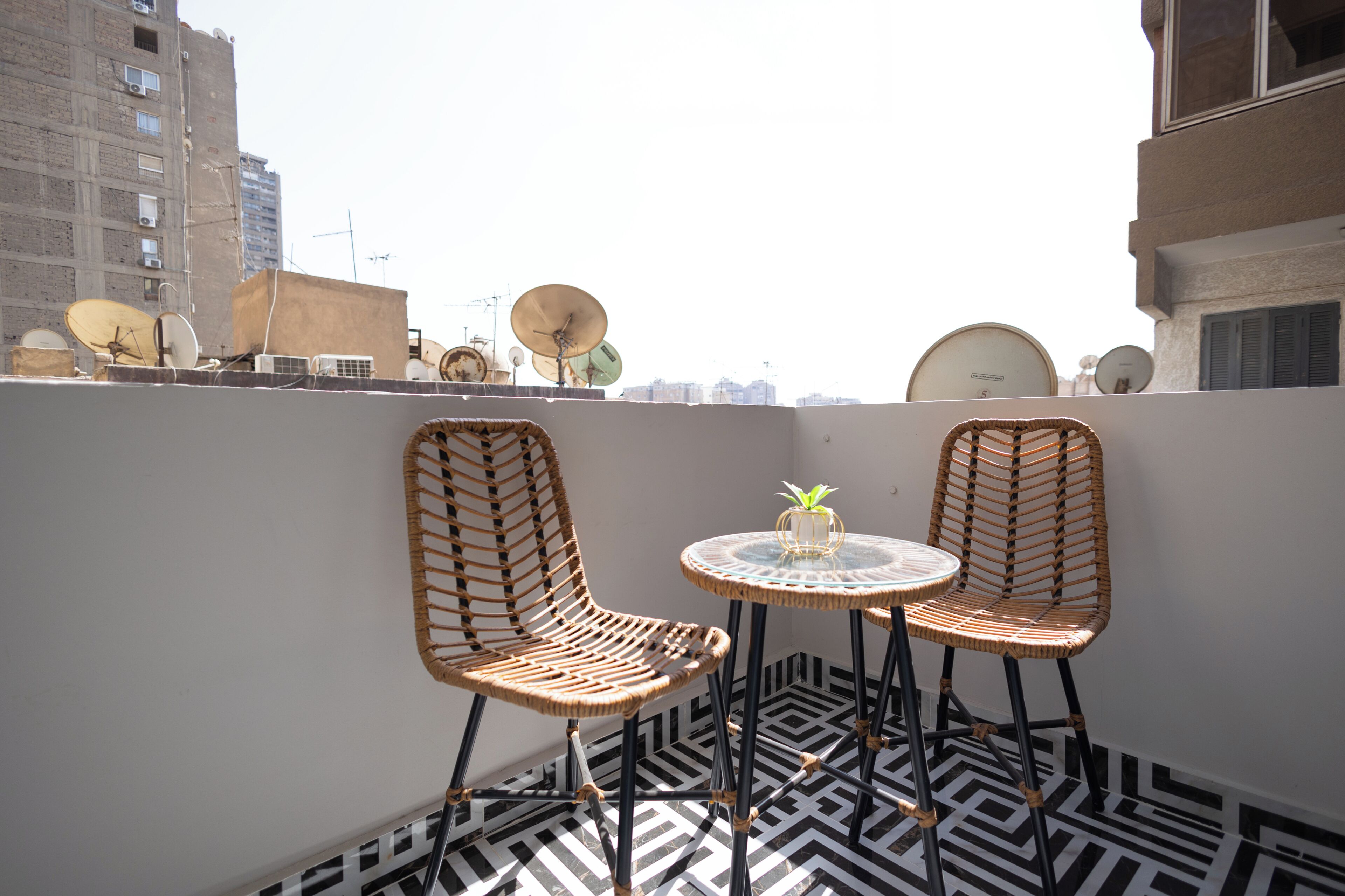 Eine Dachterrasse mit zwei Korbstühlen, einem kleinen runden Tisch und einem Blumentopf.