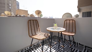 Eine Dachterrasse mit zwei Korbstühlen, einem kleinen runden Tisch und einem Blumentopf.