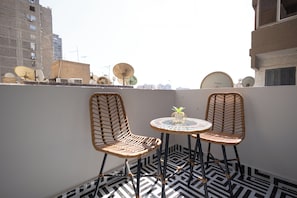Eine Dachterrasse mit zwei Korbstühlen, einem kleinen runden Tisch und einem Blumentopf.