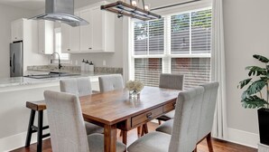 A modern kitchen with white cabinets, a stainless steel refrigerator, and a dining area with a wooden table and grey upholstered chairs. - New Thunderbolt Cottage on Harris Street Less than 4 Miles from Forsyth Park! (Savannah)