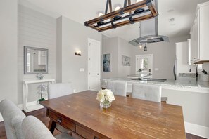 Une cuisine moderne avec un plan de travail en marbre, une table à manger en bois ornée d’un vase de fleurs et un luminaire suspendu.