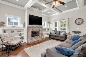A living room with a brick fireplace, a flat-screen TV, a sofa, and a chair. - New Thunderbolt Cottage on Harris Street Less than 4 Miles from Forsyth Park! (Savannah)