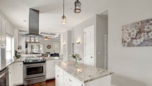 A modern kitchen with white cabinetry, a granite countertop, stainless steel appliances, and pendant lighting. - New Thunderbolt Cottage on Harris Street Less than 4 Miles from Forsyth Park! (Savannah)
