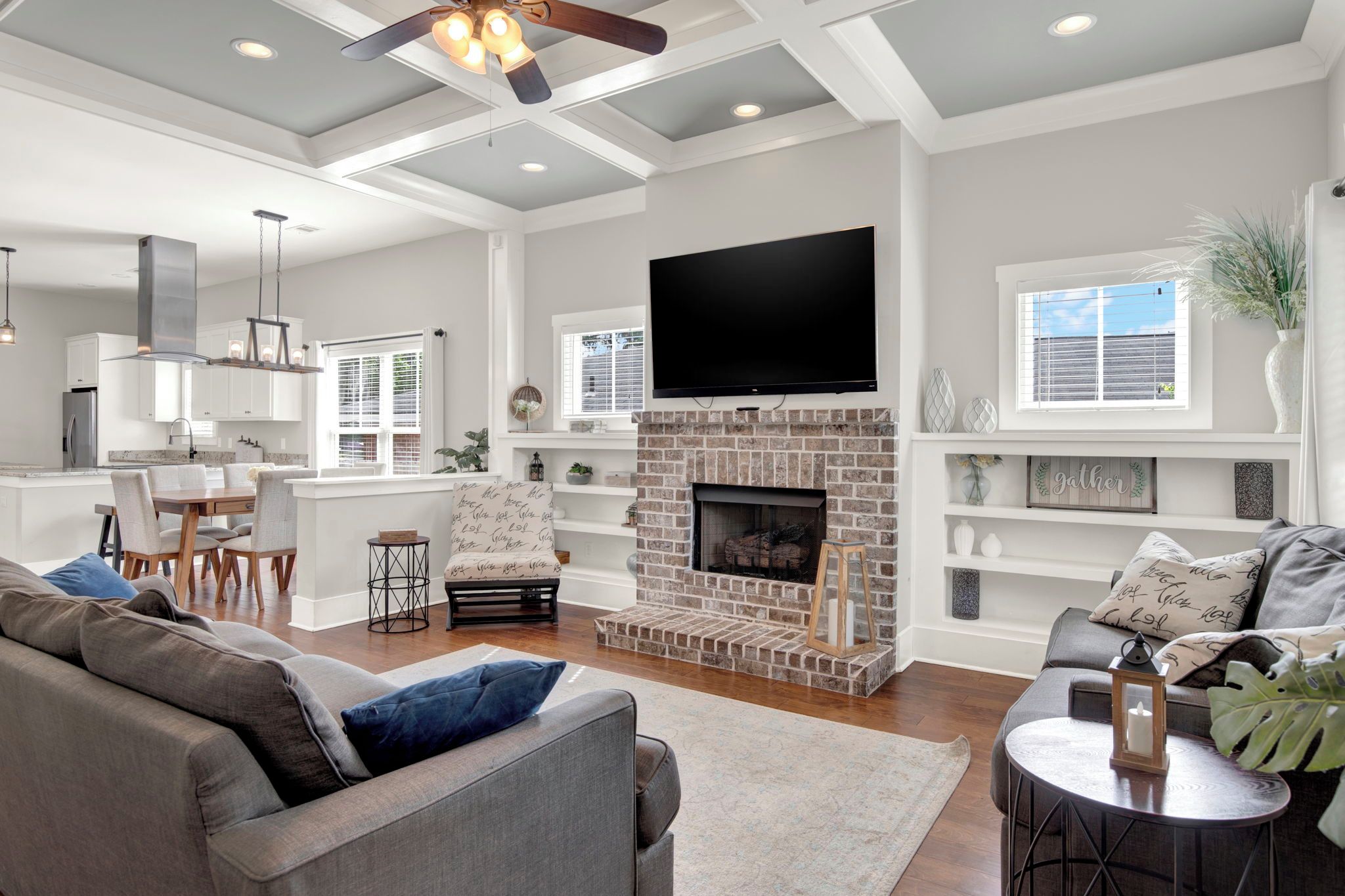 A modern living room with a fireplace, a flat-screen TV, and a dining area with a kitchen in the background.