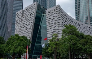 A modern building with a unique angular design, surrounded by trees and other tall buildings. - (Guangzhou)