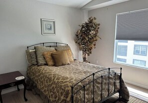 A bedroom with a bed, a nightstand, a large window with blinds, and a decorative plant. - Paradise awaits! Straight shot to the beach! Close to all Naples has to offer! (Naples)