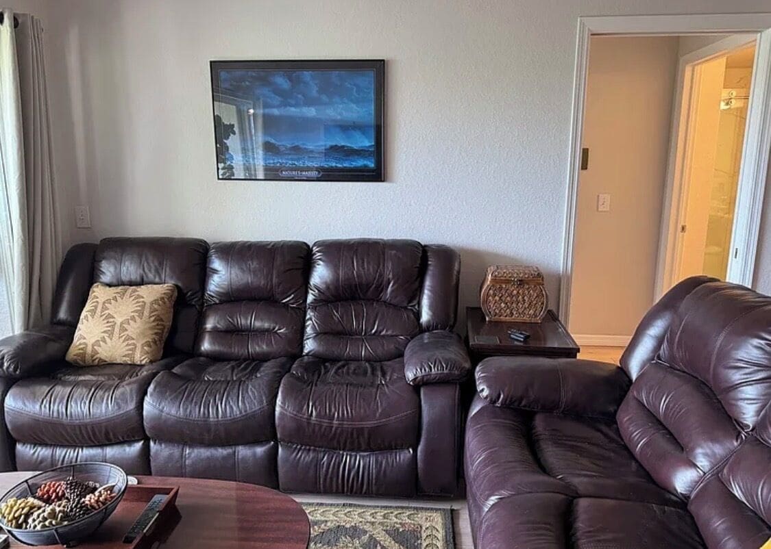 A living room with a dark brown leather sofa, a framed picture on the wall, and a small table with a decorative item.