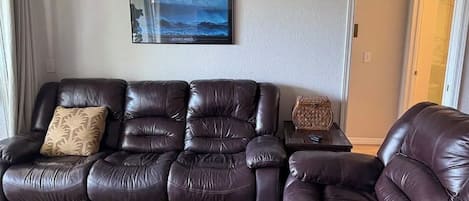 A living room with a dark brown leather sofa, a framed picture on the wall, and a small table with a decorative item.