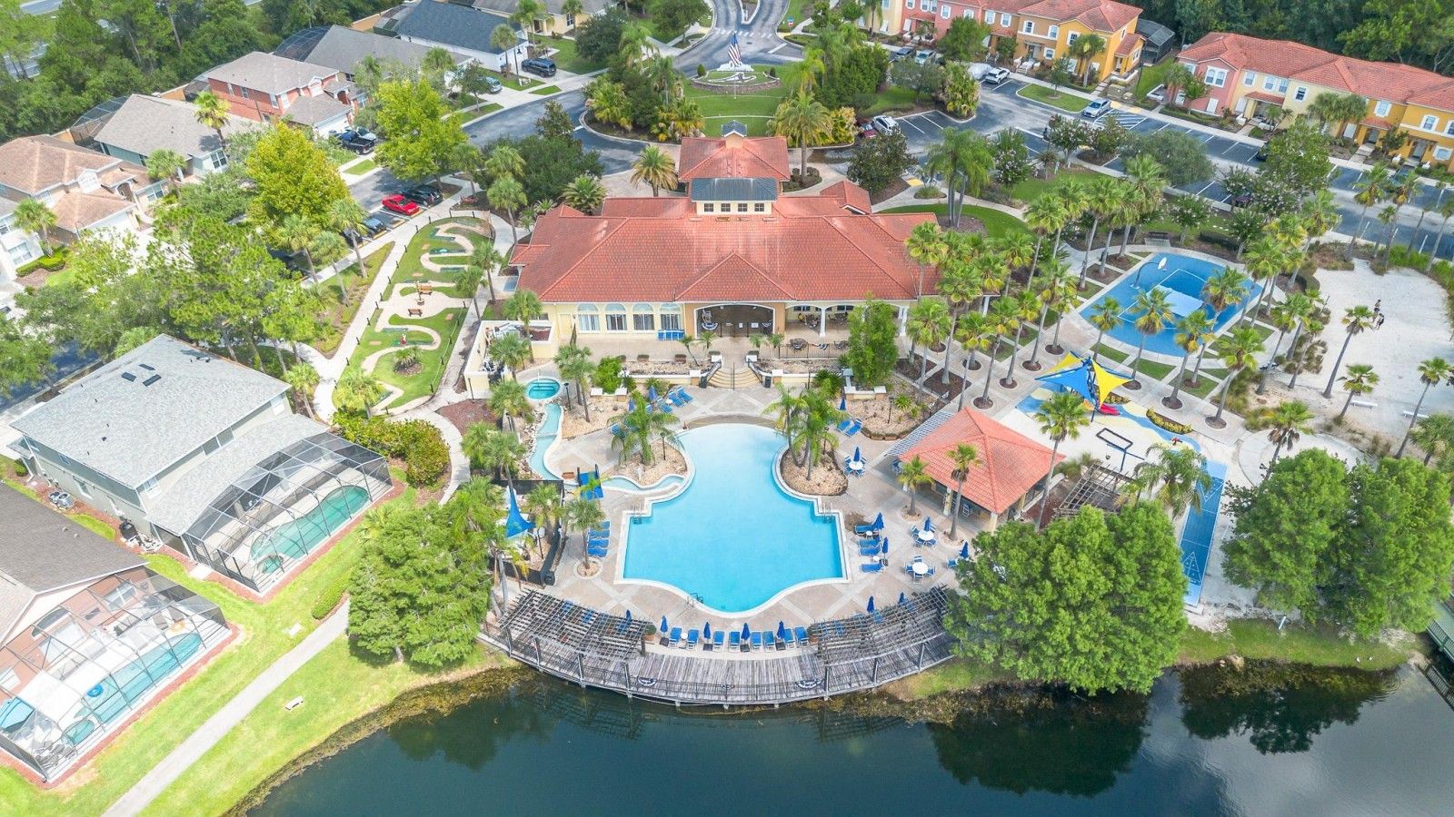 An aerial view of a resort with a central swimming pool, a covered deck area, and surrounding greenery.
