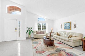 A spacious living room with two sofas, a coffee table, a potted plant, and a large window. - Magical 4BR Home w/ Pvt Pool/ Spa Near Disney 128 (Kissimmee)