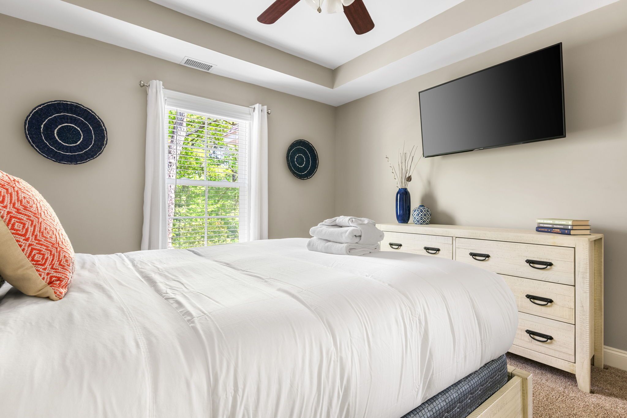 A bedroom with a bed, a dresser, a flat-screen TV, and a window with blinds.