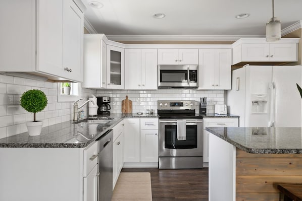 A modern kitchen with white cabinets, stainless steel appliances, a granite countertop, and a small potted plant.