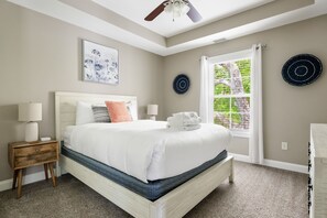 Quarto com cama, mesas de cabeceira, ventoinha no teto e janela com cortinas.