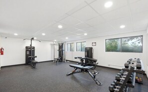 Ein Fitnessraum mit verschiedenen Trainingsgeräten, einer Bank und Kurzhanteln.