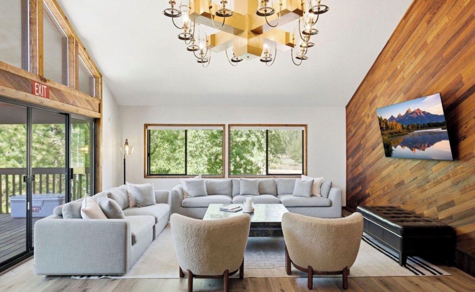 Una sala de estar moderna con un sofá modular, dos sillones, una mesa de centro y una chimenea. Amplias ventanas ofrecen luz natural y vistas al exterior.