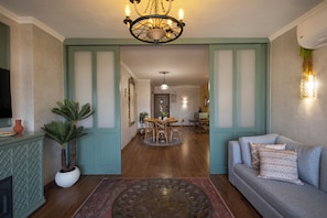 Un salon avec un canapé, une table basse et un téléviseur. On aperçoit à l’arrière-plan un coin repas avec une table et des chaises.