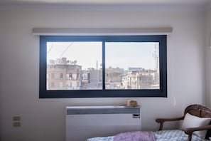 A room with a large window, an air conditioning unit, a bed with patterned bedding, and a wooden chair. - Cairo Tower View 2-Bedroom Apartment In Tahrir Square (Cairo Governorate)