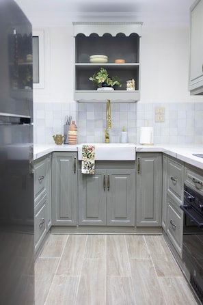 Cozinha com armários cinzas, bancada branca e painel de azulejos.
