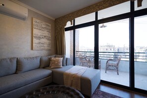 A modern living room with a grey sofa, a patterned throw blanket, and a view of the city through large windows. - Cairo Tower View 2-Bedroom Apartment In Tahrir Square (Cairo Governorate)