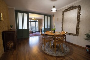 Un coin repas avec une table ronde, des chaises, un lustre et un grand miroir décoratif accroché au mur.