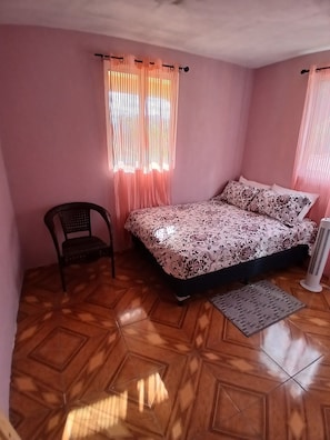 Ein Schlafzimmer mit einem Bett, einem Sessel, einem Heizkörper und einem fenster mit Vorhängen.