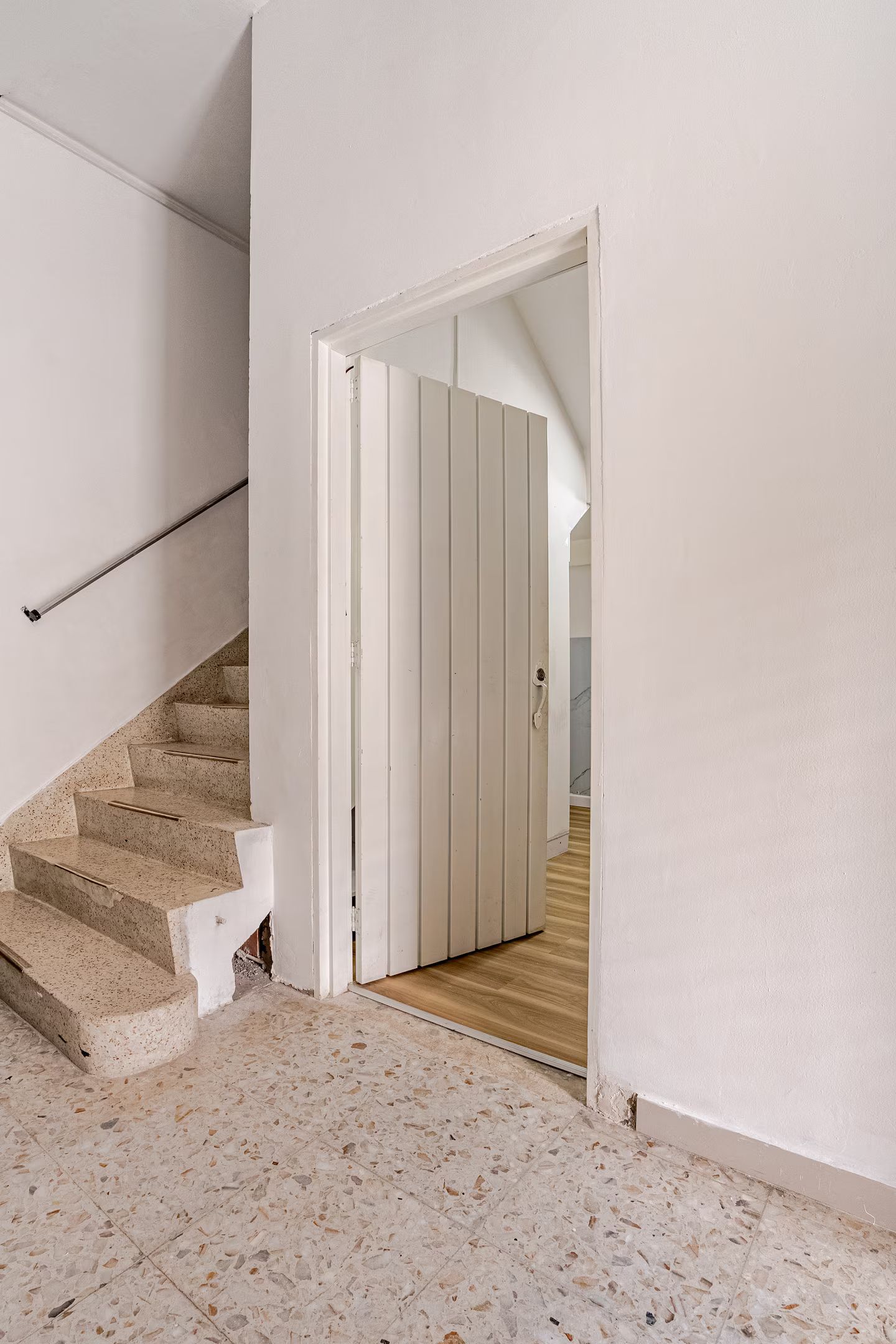 A staircase leading to a room with a wooden floor and a white door.