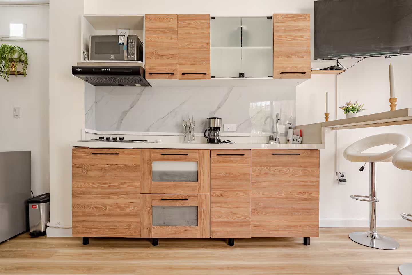 A modern kitchen with wooden cabinets, a microwave, a coffee maker, and a bar stool.