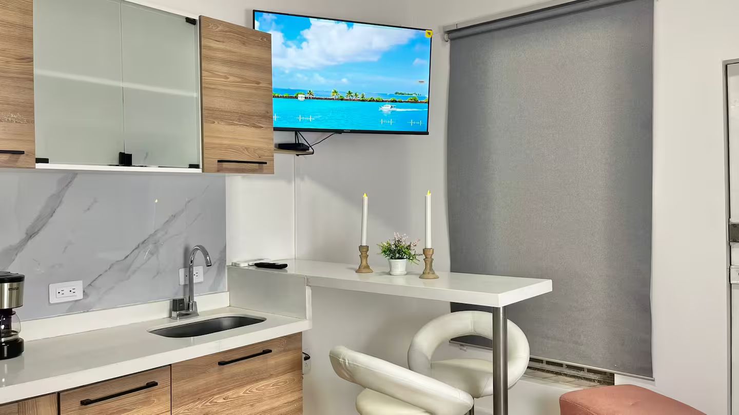 A modern bathroom with a built-in sink, a mirror, a television mounted above the mirror, and a toilet with a white seat.