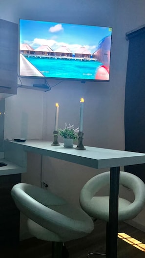 A room with a flat-screen TV mounted on the wall, two lit candles on a table, and a pair of modern chairs. - Moon house Modern Design, Comfortable & Elegant. (Cali)