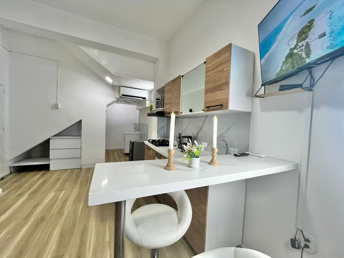 A modern kitchen with white cabinets, a white countertop, and a built-in stove. There is a white chair and a small table with candles and flowers.