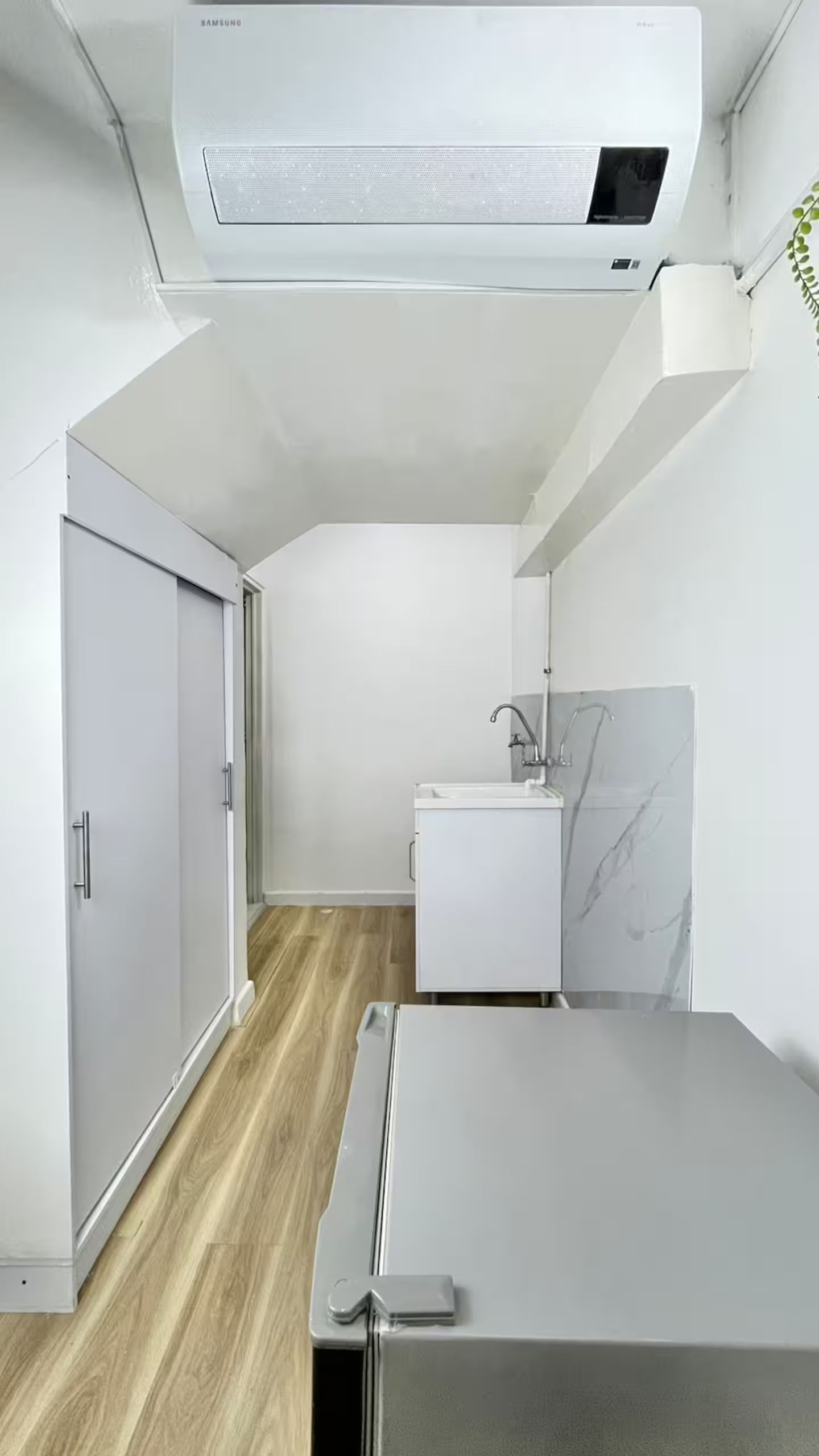 A compact room with a bed, a small sink, and a white wardrobe.